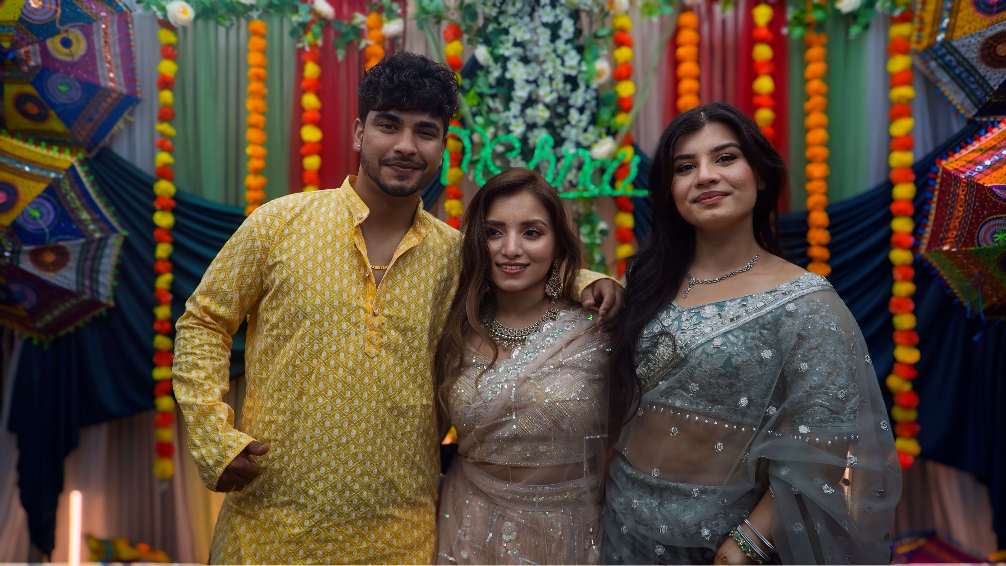 Three women at mehndi ceremony with colorful umbrellas and neon sign